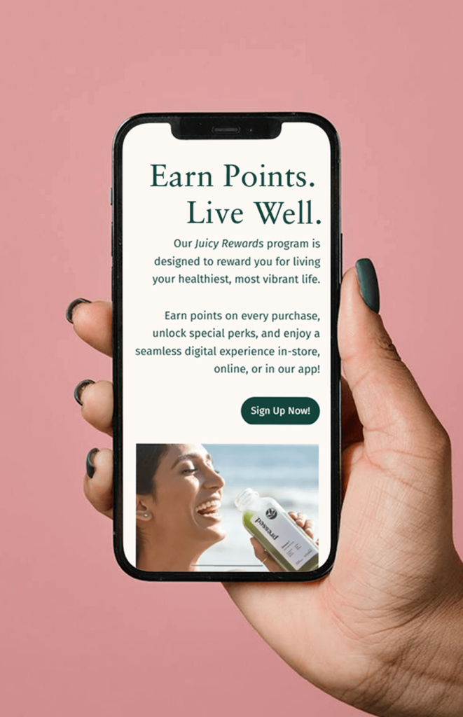 A smartphone displaying a rewards program sign-up page. The text on the screen promotes a program called Juicy Rewards, encouraging users to earn points on purchases and unlock perks. The design is clean, with a green "Sign Up Now!" button and an image of a smiling woman holding a bottled juice near the bottom. The overall aesthetic feels fresh and health-focused.